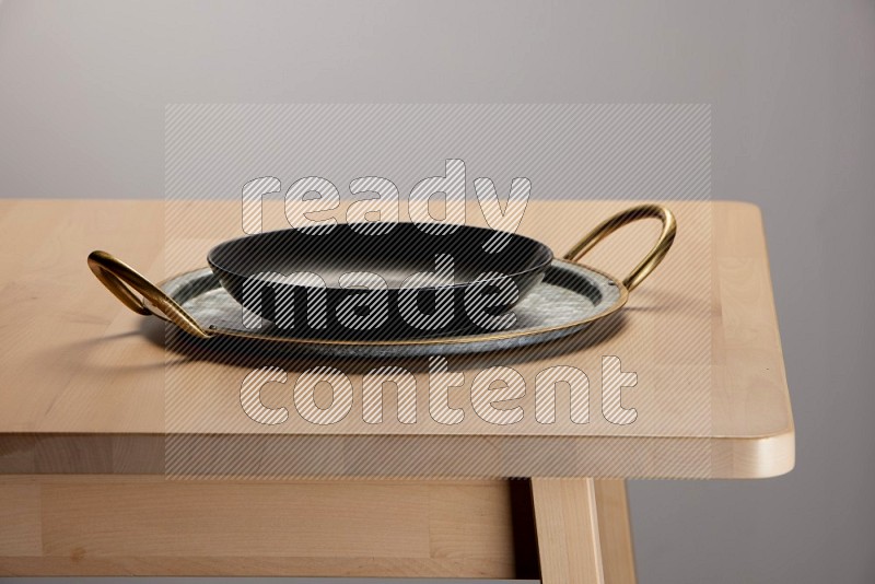 black plate placed on a rounded stainless steel metal tray with golden handels on the edge of wooden table