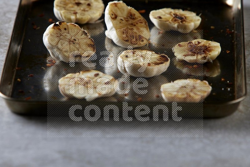 half's roasted garlic in a stainless tray on a grey textured countertop