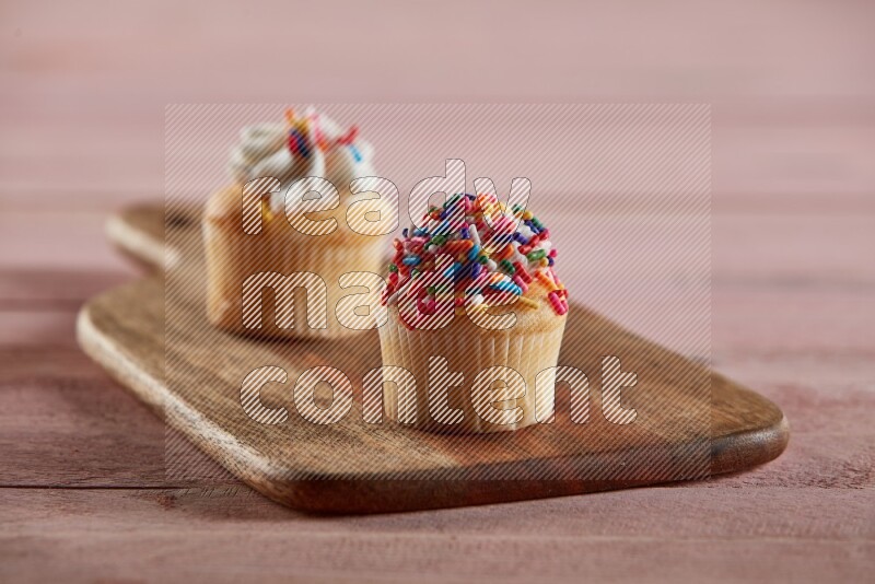 Vanilla mini cupcake topped with sprinkles on a wooden board