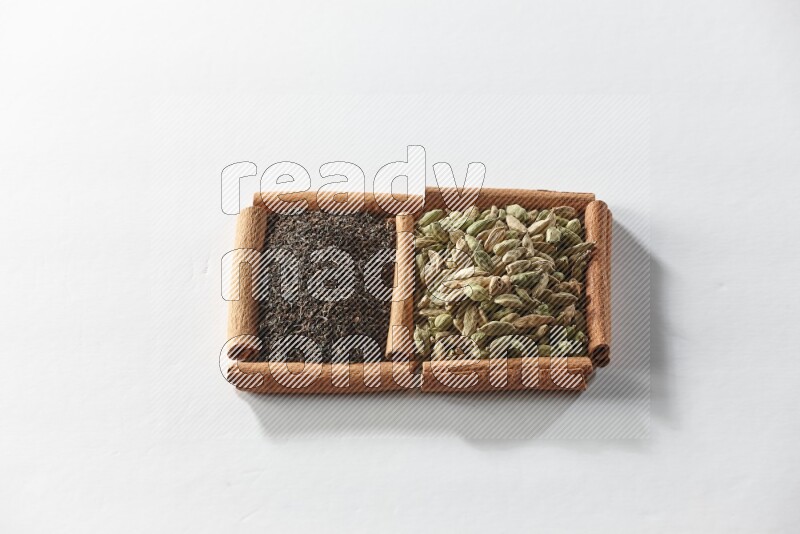 مربعان من أعواد القرفة ممتلئان بحبوب الهيل والشاي الأسود علي خلفية بيضاء