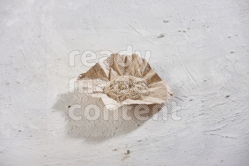 A crumpled piece of paper full of garlic powder placed on a textured white flooring