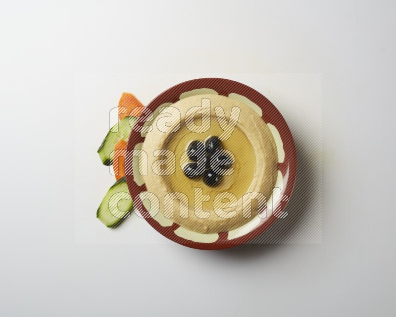 Hummus in a traditional plate garnished with black olives on a white background
