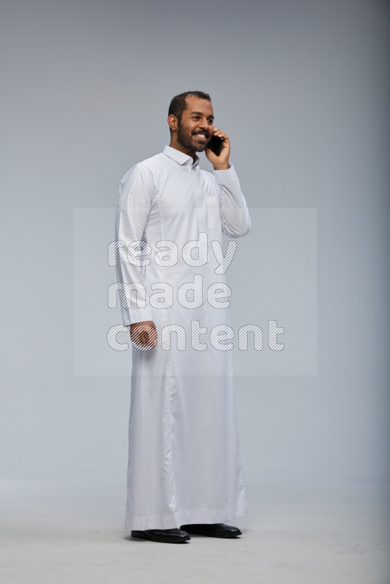 Saudi man wearing Thob standing talking on phone on Gray background