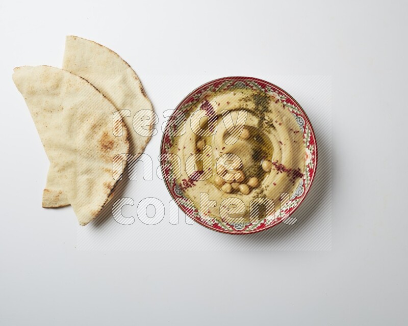 Hummus in a red plate with patterns garnished with zaatar & sumak on a white background