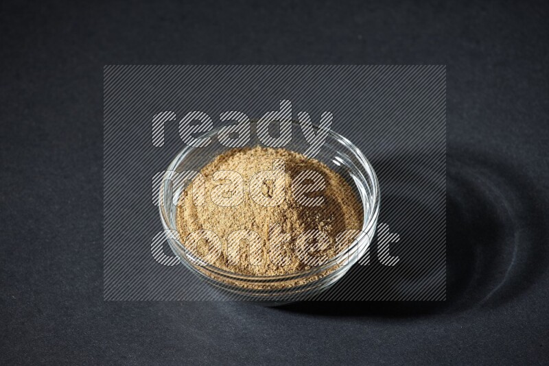 A glass bowl full of cumin powder on black flooring