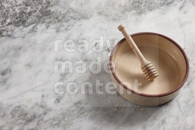 Beige Pottery oven bowl with wooden honey handle on the side with grey marble flooring, 65 degree angle