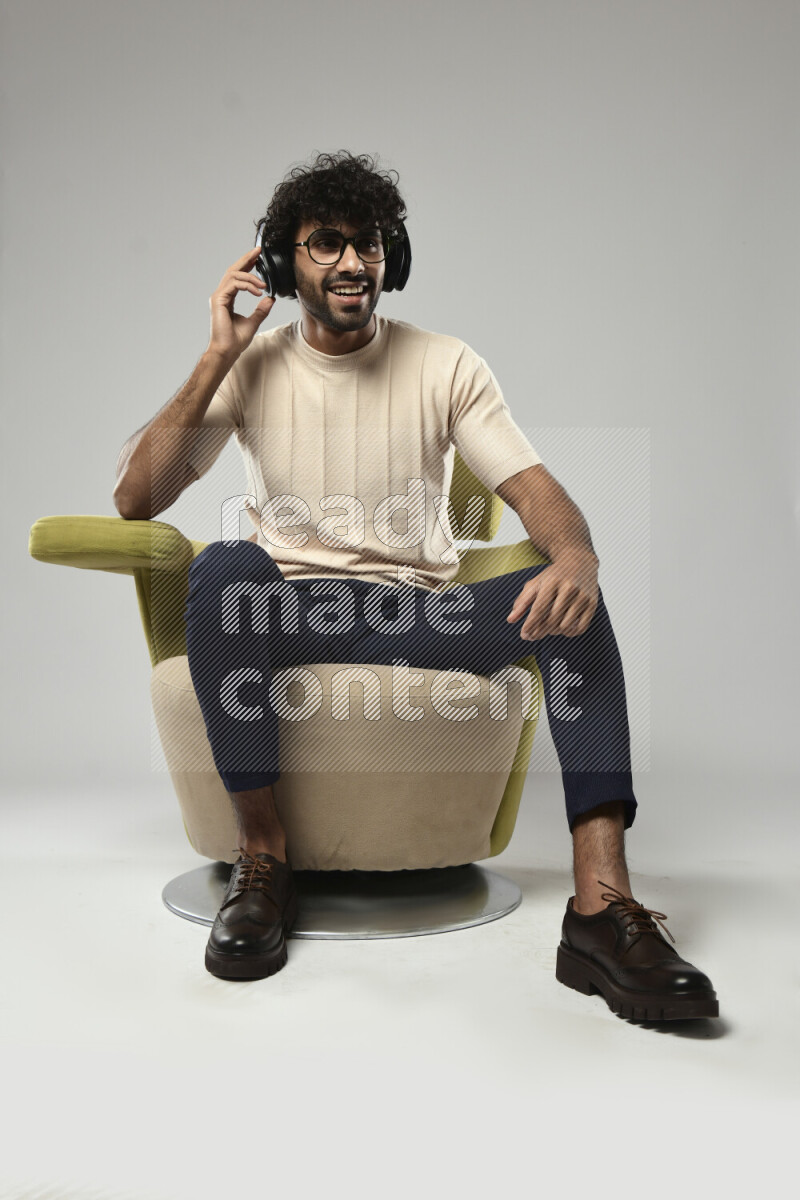 A man wearing casual sitting on a chair putting on headphones on white background