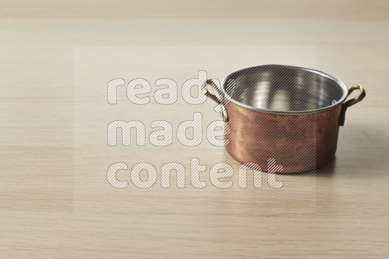 A small copper pot on light wooden background
