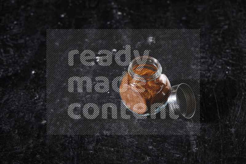 A glass jar full of ground paprika powder on black background