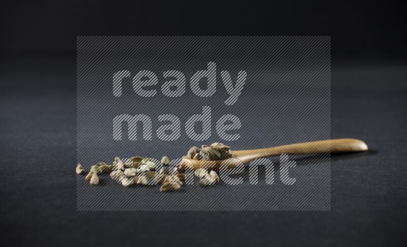 A wooden spoon full of cardamom on black flooring