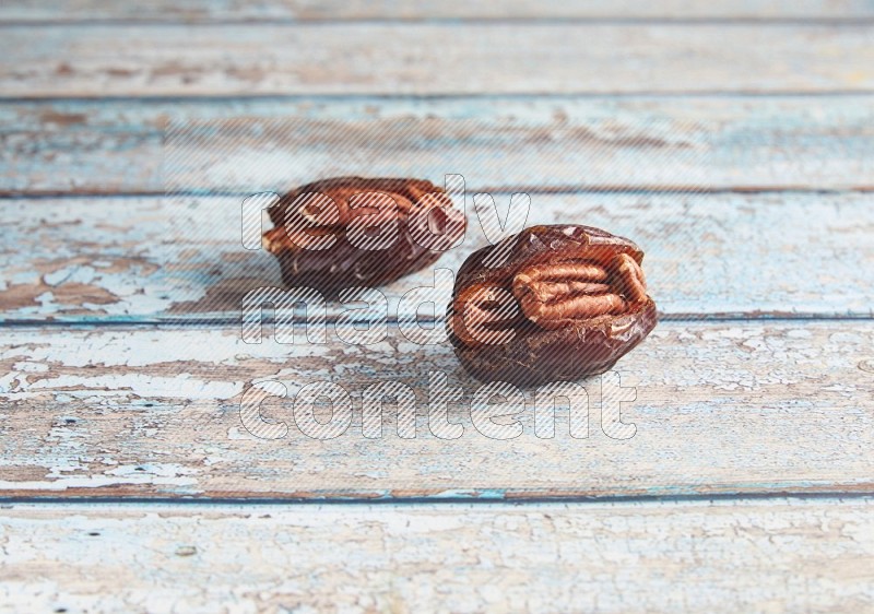 two pecan stuffed madjoul dates on a light blue wooden background