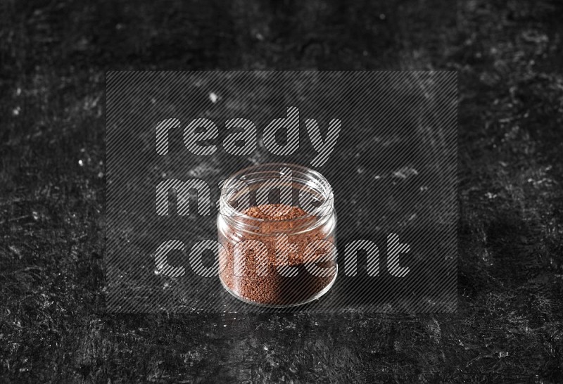 A glass jar full of garden cress seeds on a textured black flooring