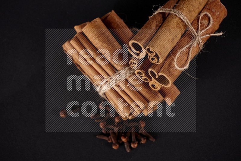 Two bounded stacks of cinnamon sticks with cloves on black background