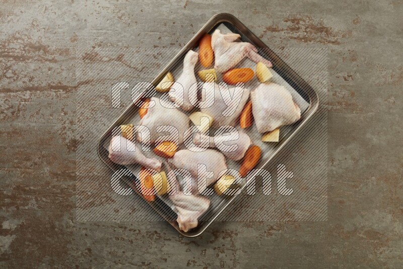 Mixed fresh chicken pieces in an oven tray on a textured rustic background