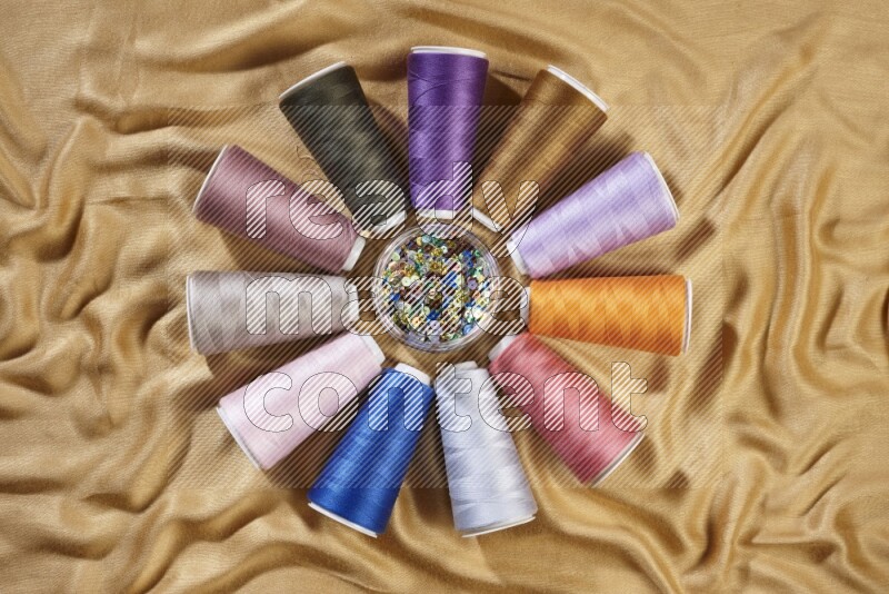 Multicolored sewing thread spools on yellow fabric background