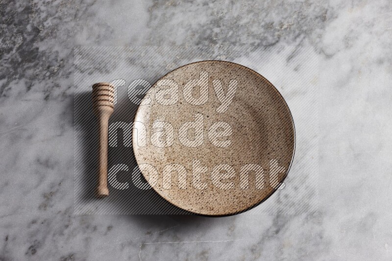 Multicolored pottery plate with wooden honey dipper on the side on grey marble background