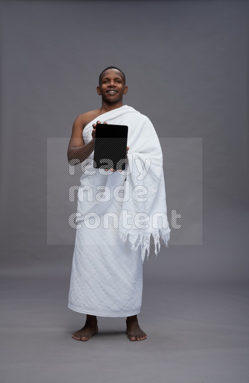 A man wearing Ehram Standing showing tablet to camera on gray background