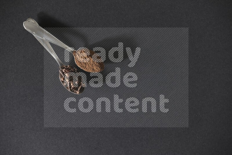 ملعقتان معدنيتان، إحداهما ممتلئة بحبوب القرنفل والأخرى ببودرة القرنفل، على خلفية سوداء