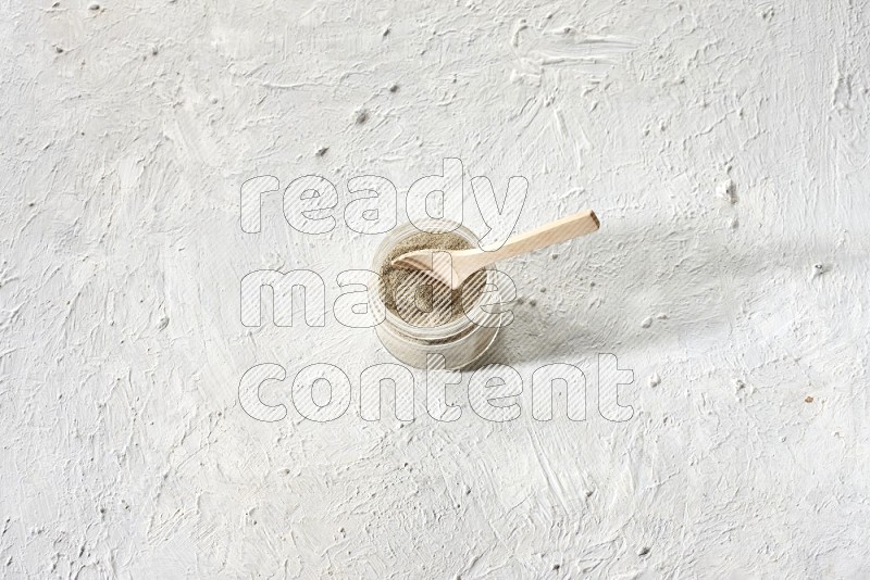 وعاء زجاجي وملعقة خشبية ممتلئان ببودرة الفلفل الأبيض على أرضية بيضاء