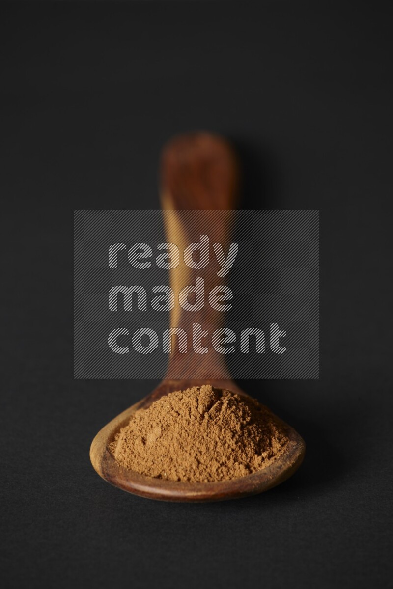 Cinnamon powder in a spoon ladle on black background