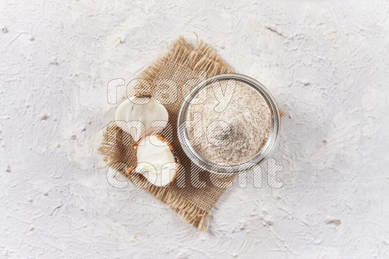 A glass bowl full of onion powder on burlap fabric on white background