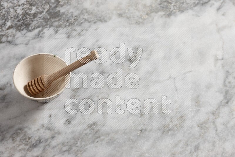 Beige pottery bowl with wooden honey dipper in it on grey marble background