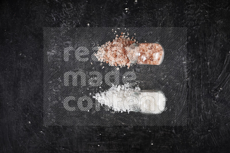 2 وعاء زجاجي احدهمها ممتلئ بملح الهيمالايا الخشن والأخر بملح البحر الخشن على خلفية سوداء