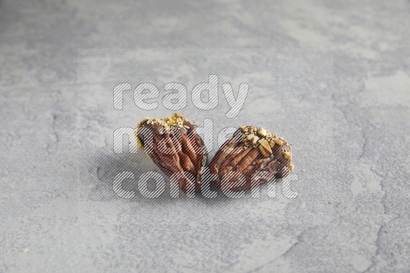 Two pecan stuffed dates covered with Dark chocolate and chopped pistachios on alight grey background