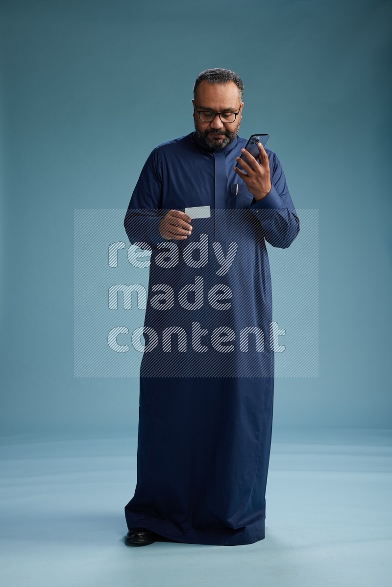 Saudi Man without shimag Standing holding ATM while talking on phone on blue background