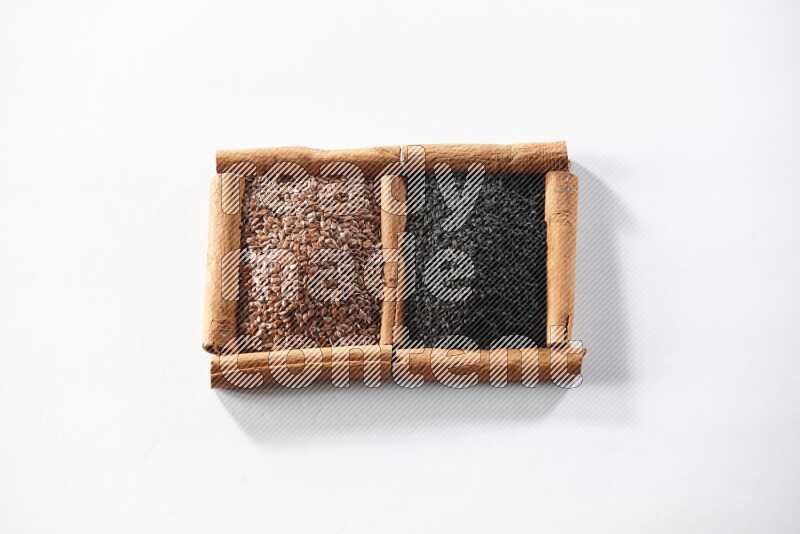 مربعان من أعواد القرفة ممتلئان ببذور الكتان وحبة البركة السوداء علي خلفية بيضاء