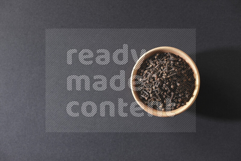 A wooden bowl full of cloves on a black flooring