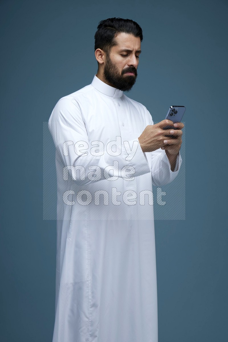 A man Texting in a blue background wearing Saudi Thob