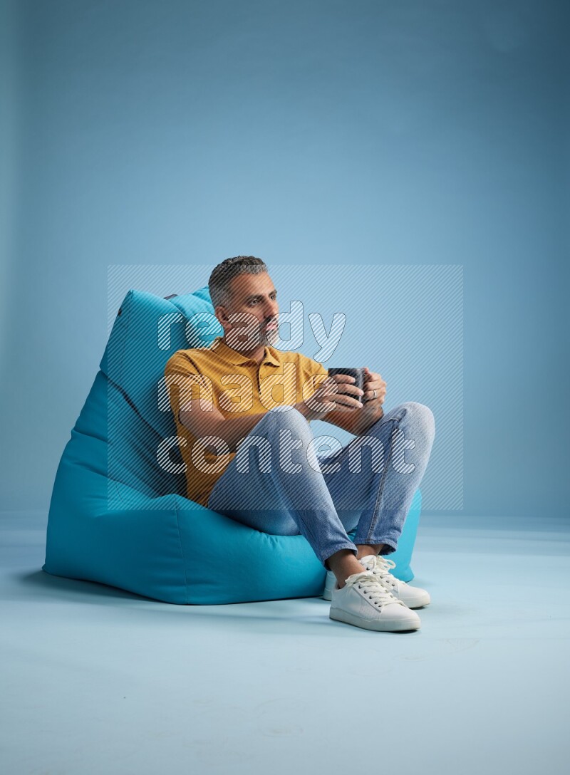 A man sitting on a blue beanbag and drinking coffee