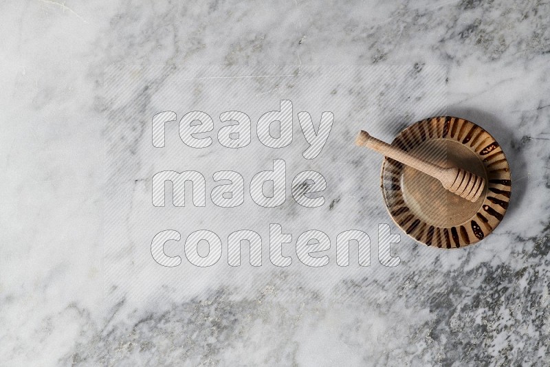 Multicolored Pottery Plate with wooden honey handle in it, on grey marble flooring, Top View