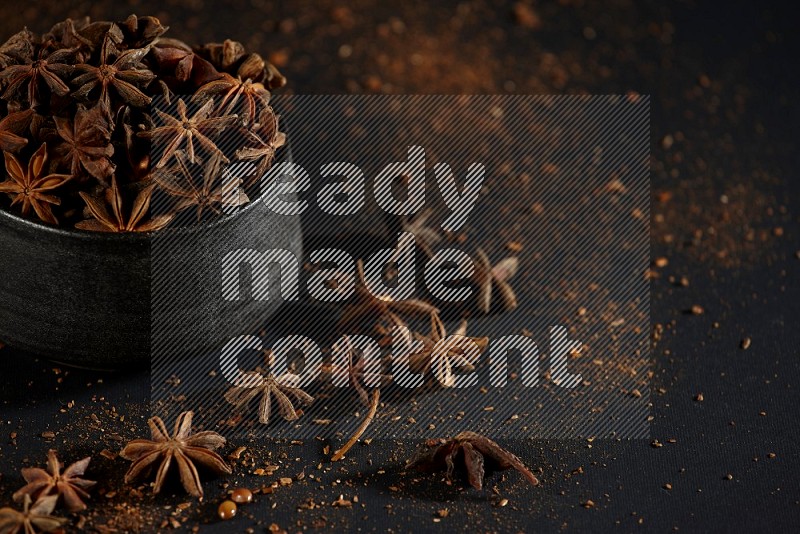 Star Anise in a black bowl with sprinkled anise on black flooring