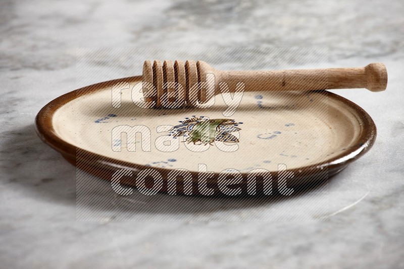 Decorative Pottery Plate with wooden honey handle in it, on grey marble flooring, 15 degree angle