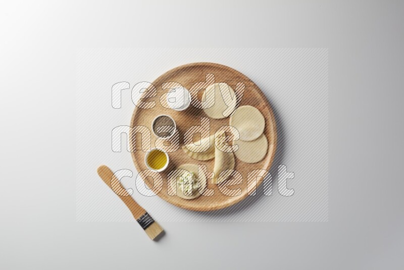 two closed sambosas and one open sambosa filled with cheese while salt, black pepper and oil with oil brush aside in a wooden dish on a white background