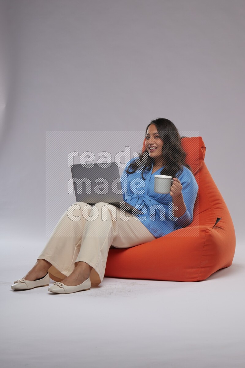 A woman sitting on an orange beanbag and working on laptop
