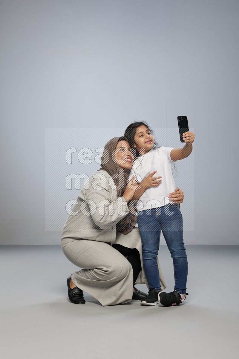 A girl standing taking selfie with her mother on gray background