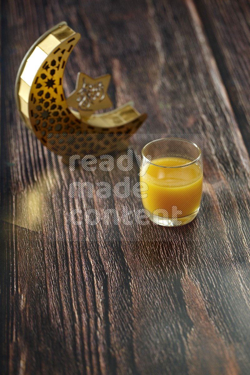فانوس خشبي هلالي باللون الذهبي مع مشروبات مختلفة وتمر ومكسرات وسبحة صلاة وقرآن على خلفية خشبية بنية