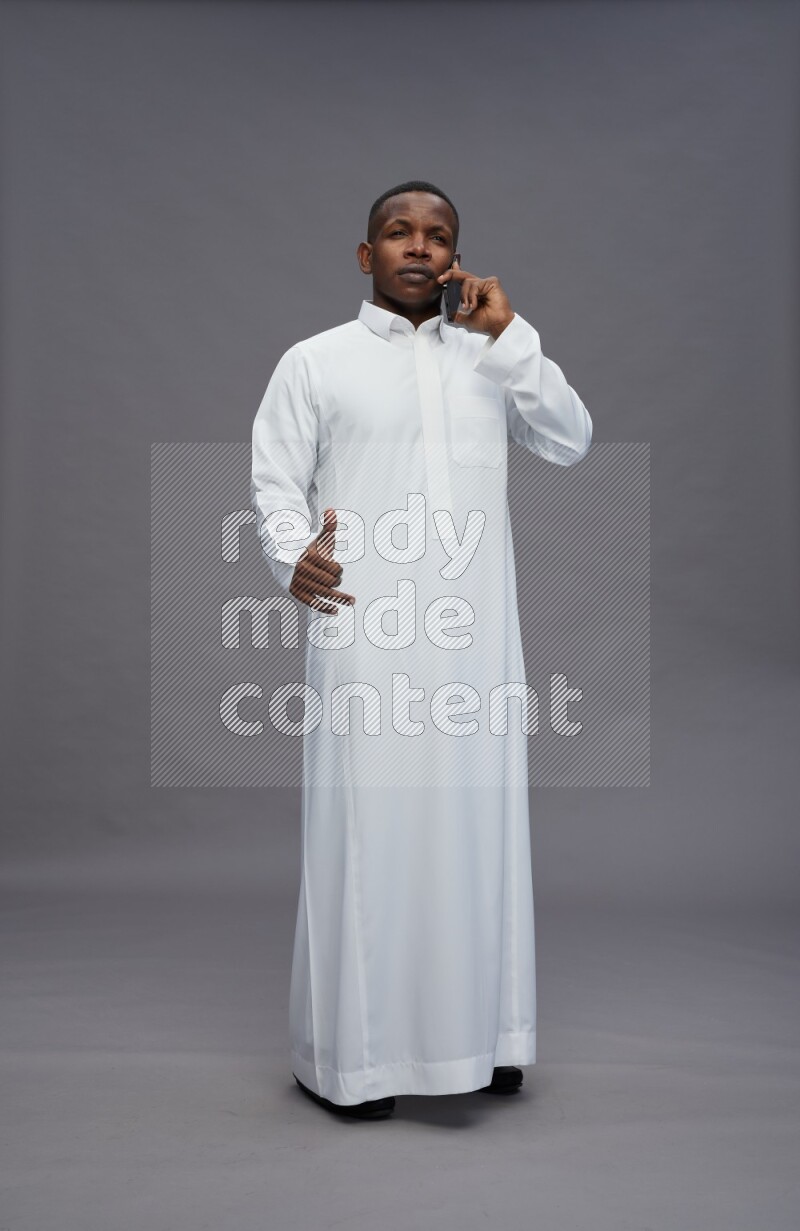 Saudi man wearing thob standing talking on phone on gray background