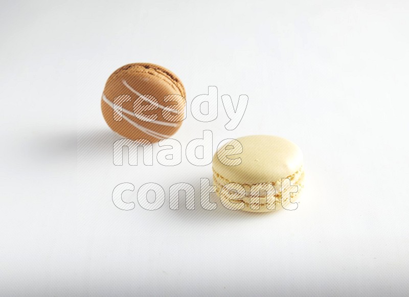 45º Shot of of two assorted Brown Irish Cream, and Yellow Vanilla macarons on white background