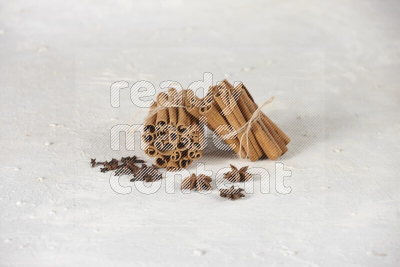 Two bounded stacks of cinnamon sticks with cloves and star anise on white background