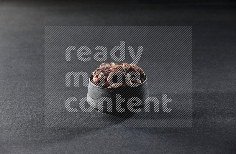 A black pottery bowl full of dried dates on a black background in different angles