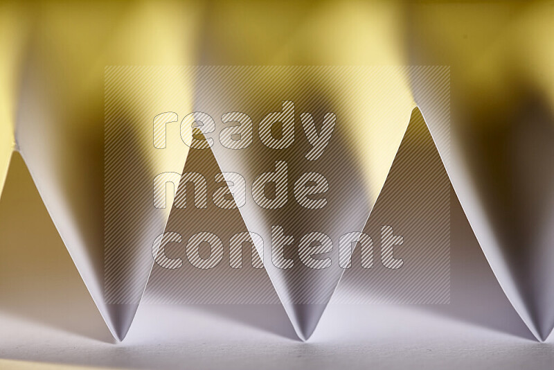 A close-up abstract image showing sharp geometric paper folds in white gradients and warm tones