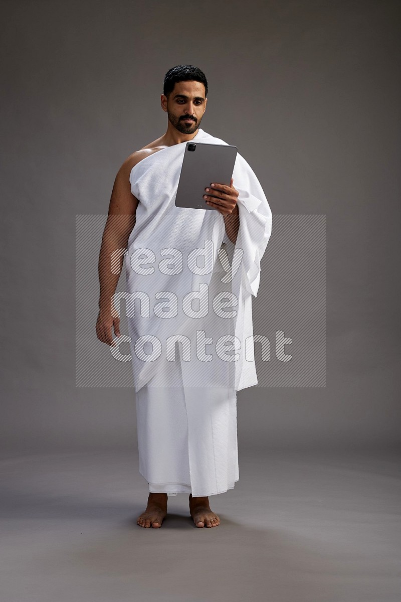 A man wearing Ehram and holding a tablet on gray background