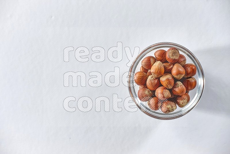 A glass bowl full of hazelnuts on a white background in different angles