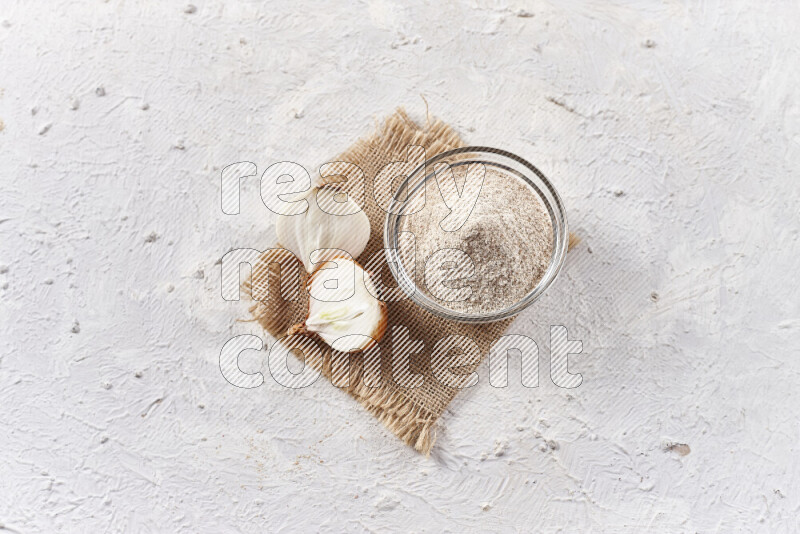 A glass bowl full of onion powder on burlap fabric on white background