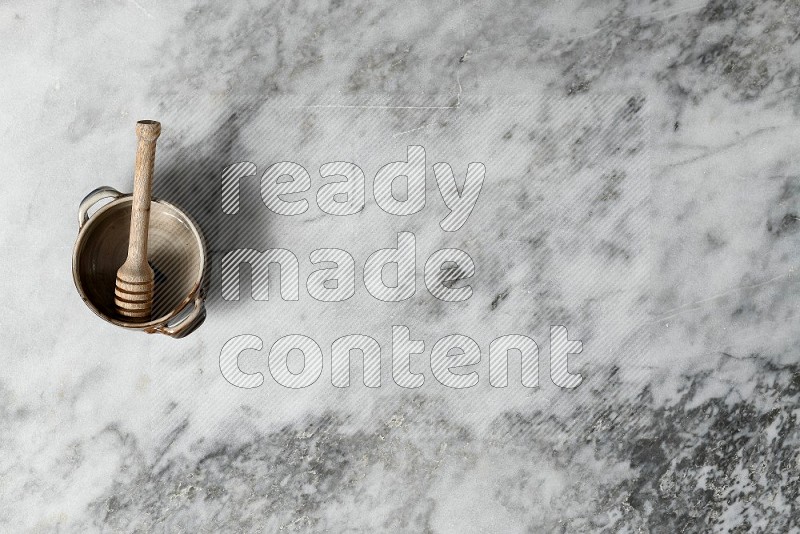 Multicolored Pottery Bowl with wooden honey handle in it, on grey marble flooring, Top View