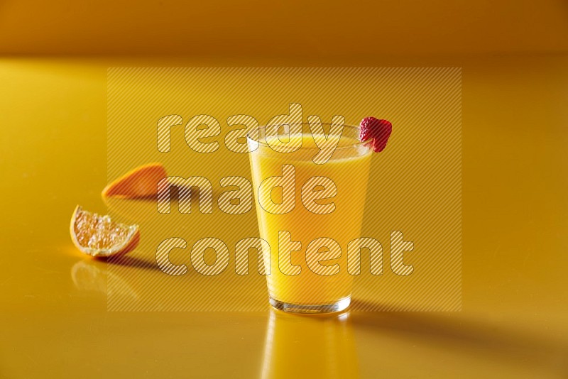 glass of orange juice with berry on yellow background